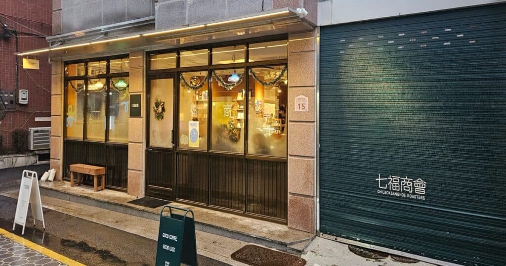 칠복상회로스터스 외관: 짙은 녹색 셔터와 금속 프레임의 빈티지한 수유 카페 입구 전경