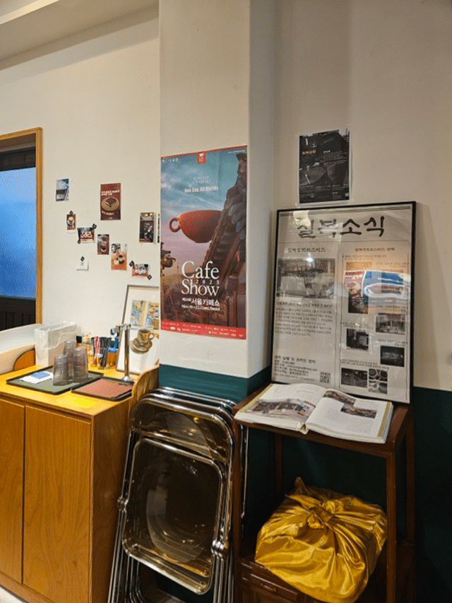칠복상회로스터스 실내: 커피쇼 포스터와 신문 스크랩이 있는 원목 수납장 및 접이식 의자
