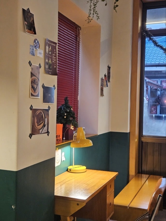 칠복상회로스터스 인테리어 디테일: 노란색 스탠드 조명과 미니 트리가 있는 빈티지한 책상 코너