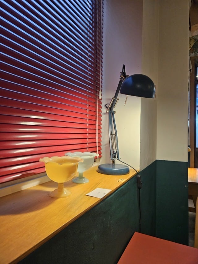 칠복상회로스터스 창가: 빨간 블라인드와 빈티지한 유리 그릇, 파란색 스탠드 조명