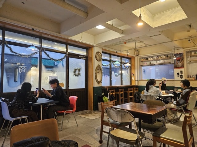 칠복상회로스터스 창가 좌석: 창밖 풍경과 실내 테이블에 앉아있는 손님들