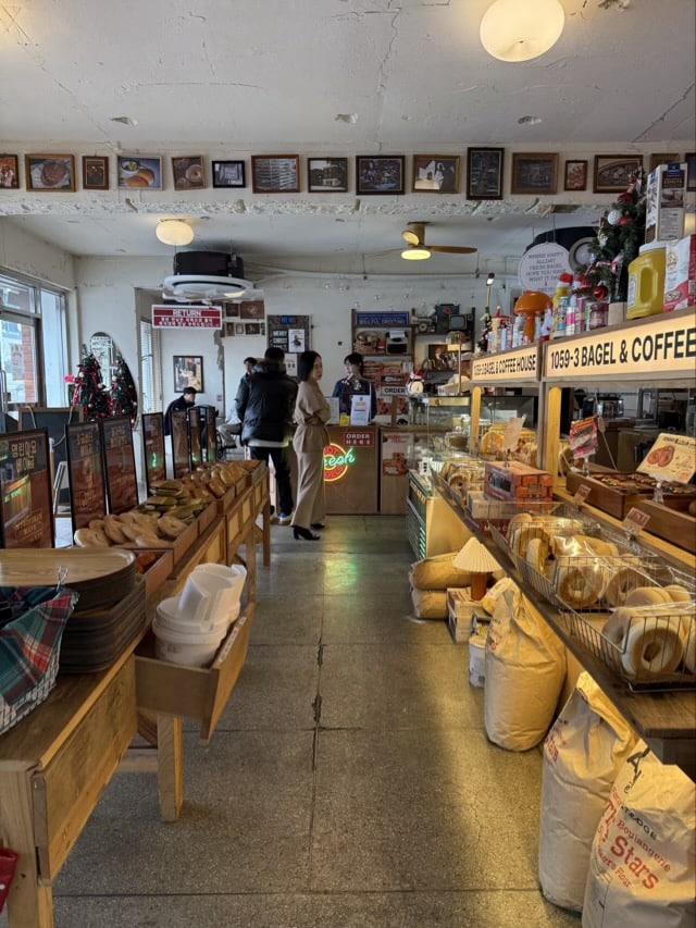 수원 권선동 베이글 커피하우스 내부, 베이글 진열대와 카운터, 손님들이 서있는 모습.