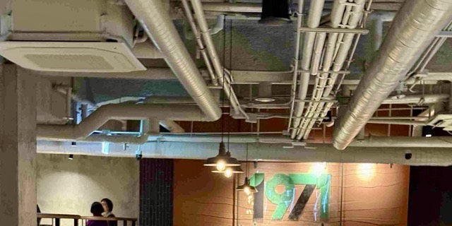 배관과 콘크리트 구조가 드러난 노출 천장 인테리어, 따뜻한 조명이 어우러진 광장시장 스타벅스 1971 인테리어