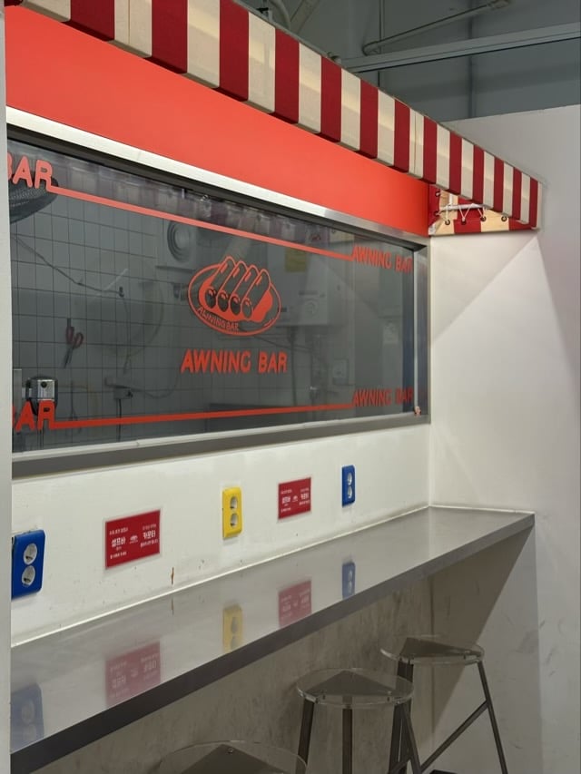 마곡 어닝바의 스테인리스(서스) 카운터와 빨강/흰색 어닝 디테일 (키치 레트로 인테리어)
