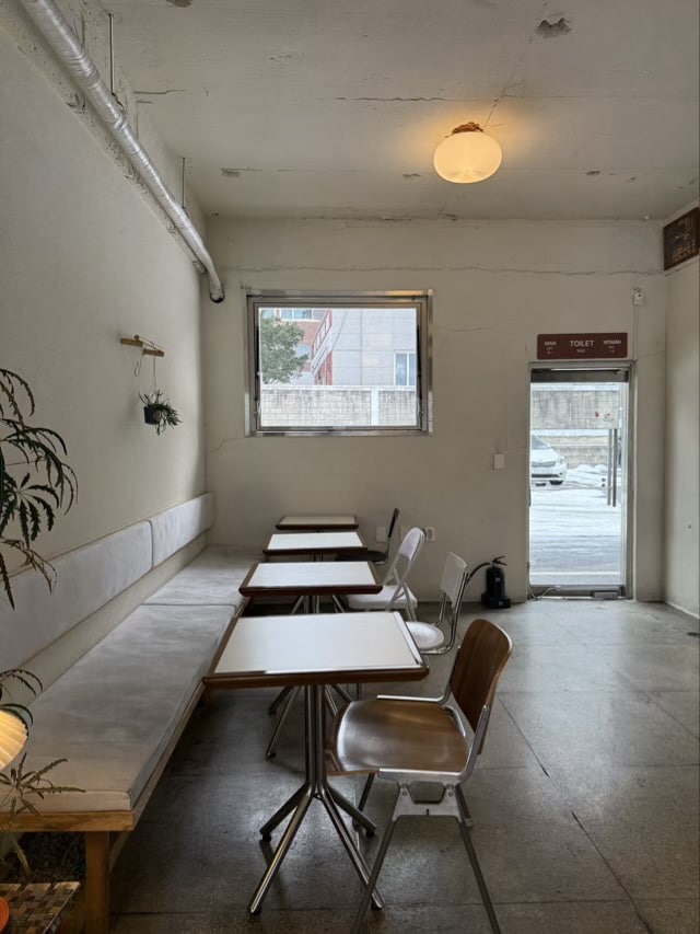 수원 권선동 베이글 커피하우스의 밝은 벽면과 벤치 좌석, 도끼다시 마감 바닥의 미니멀한 공간.