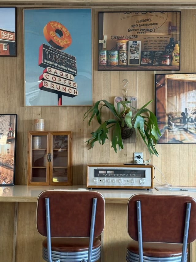 우드 벽면에 걸린 빈티지 포스터와 레트로 오디오 장치, 뿔고사리 식물이 놓인 1059-3 베이글 커피하우스 벽면.