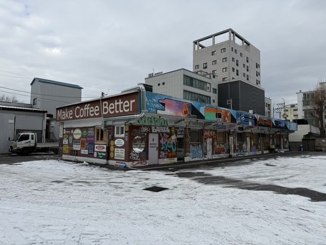 눈 덮인 주차장 앞에 위치한 수원 권선동 1059-3 베이글 커피하우스의 그래피티와 빈티지 간판으로 장식된 외관.