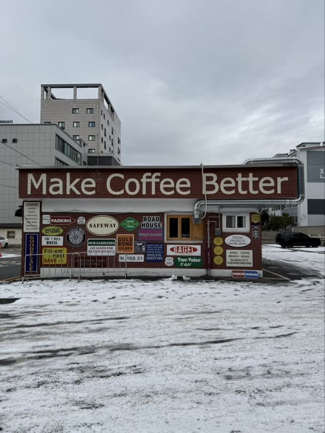 수원 권선동 베이글 커피하우스의 붉은 벽돌 외관과 'Make Coffee Better' 간판, 다양한 빈티지 스티커가 붙은 모습.