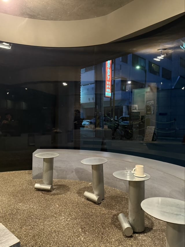 곡면 유리창 너머로 보이는 성수동 거리와 내부 금속 테이블